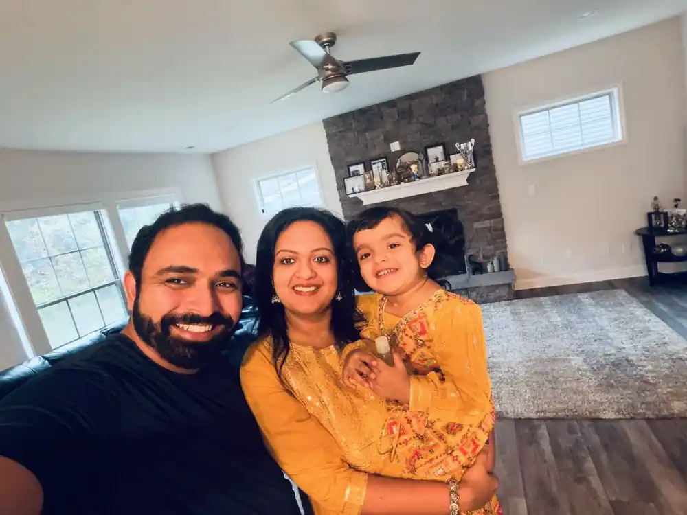 Akhil smiling in a selfie at home with his wife and young daughter