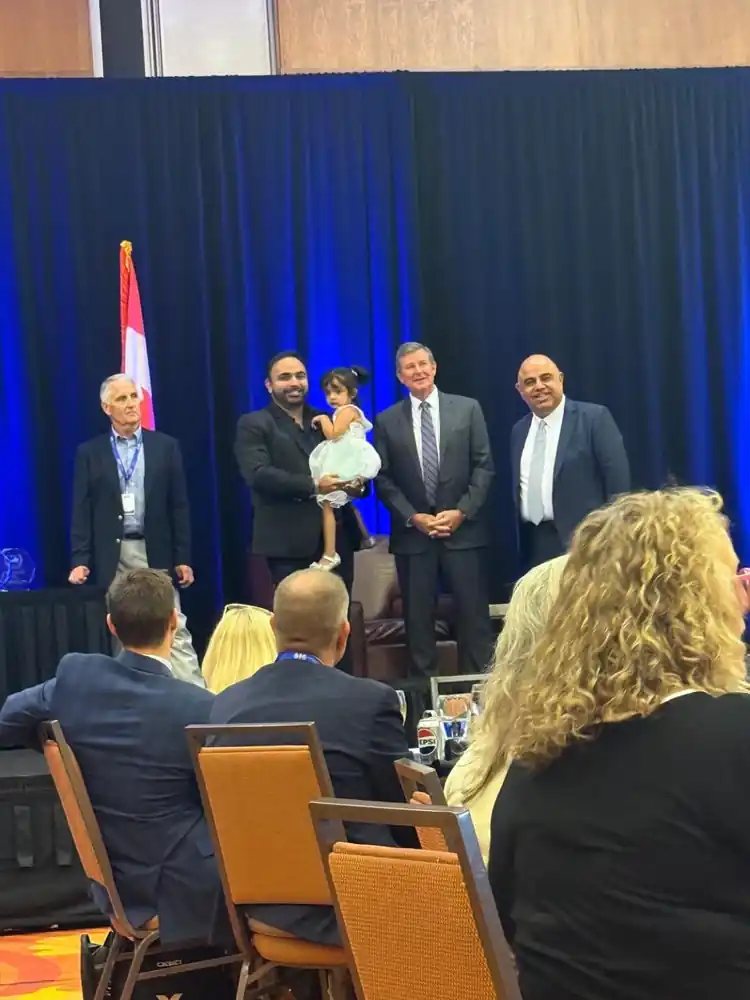 Akhil on stage with award presenters at the World Trade Center Kentucky event, guests seated in front.