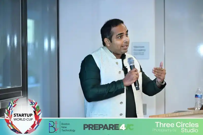 Akhil speaking into a microphone in front of a seated audience.