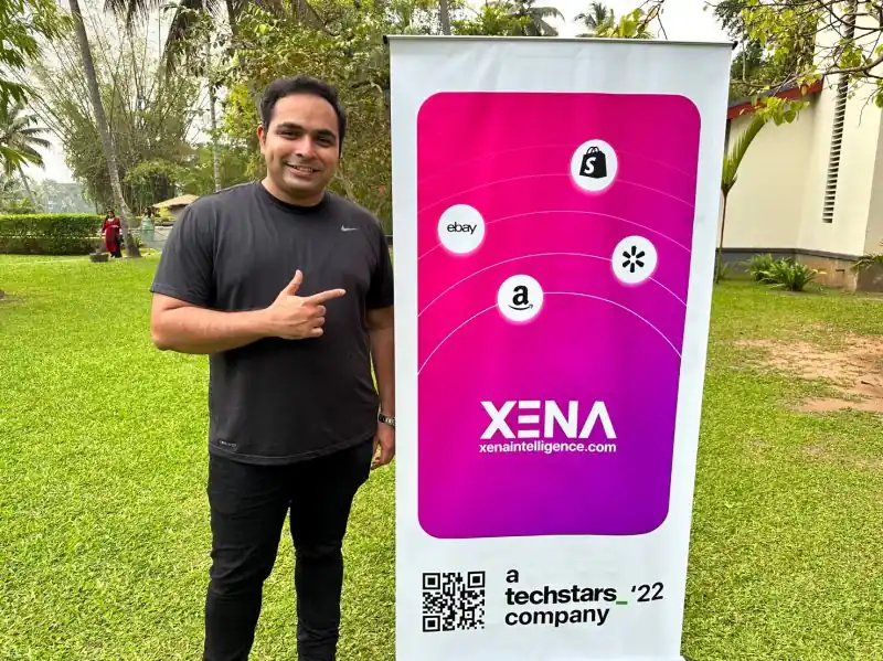Akhil pointing to a XENA Techstars '22 company banner on a lawn