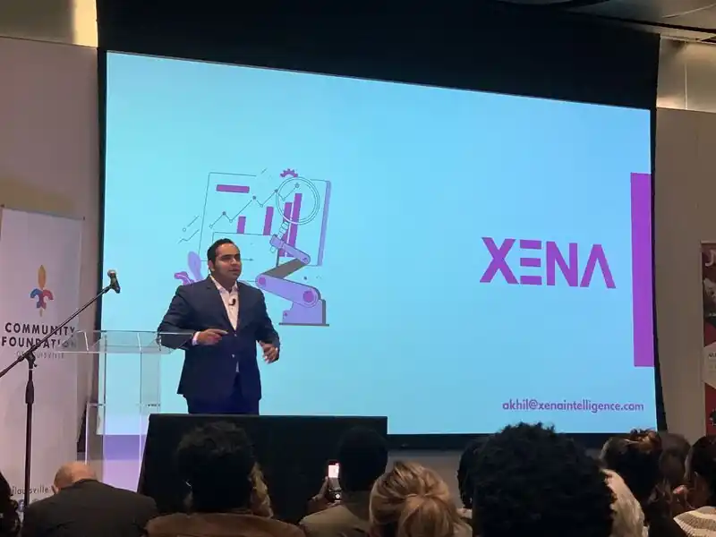 Akhil presenting on stage in front of a large XENA slide at the Vogt Awards demo day.