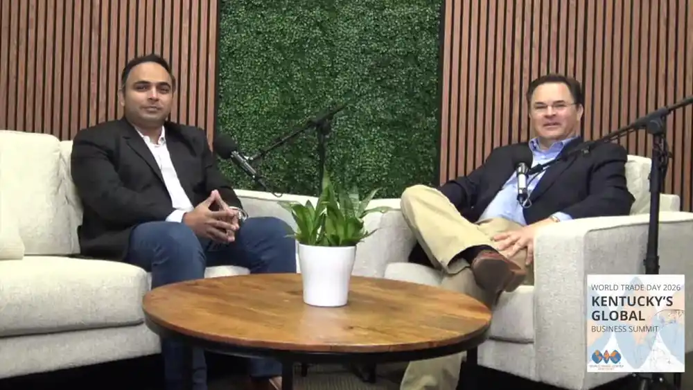 Akhil seated on a sofa in conversation with an interviewer on a World Trade Day set.